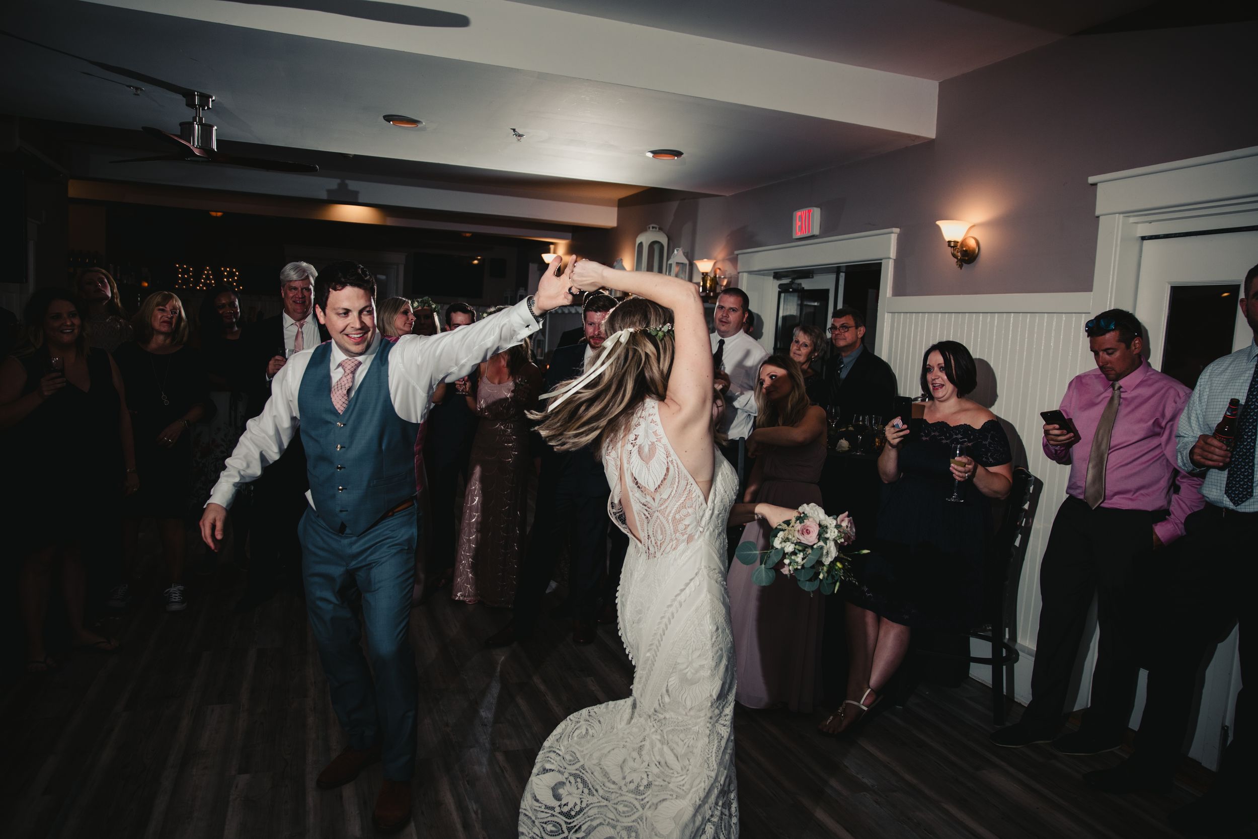 Bride and groom dancing joyfully at wedding reception while guests celebrate in elegant venue.