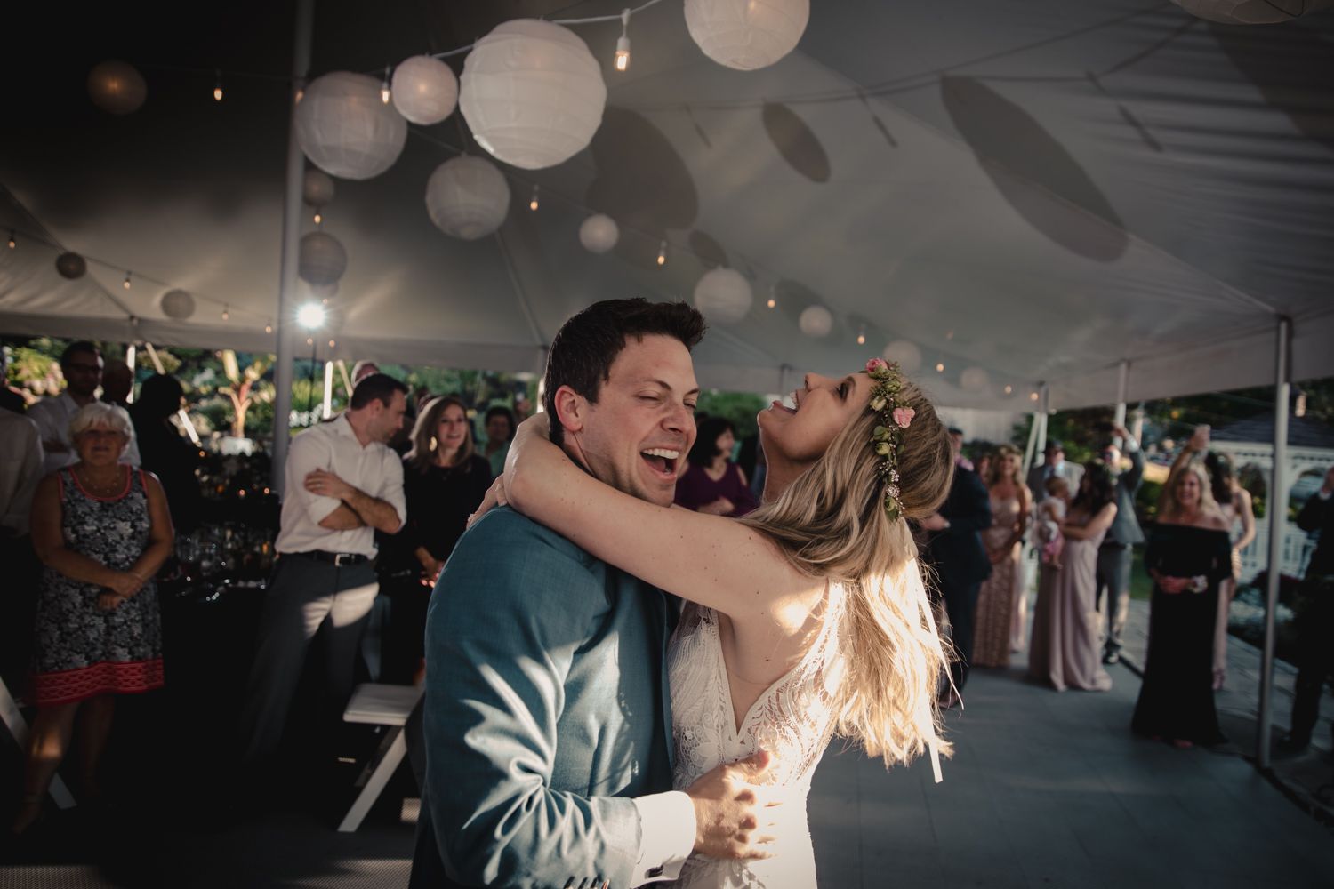 Bride and groom share a joyful first dance under white paper lanterns at an elegant outdoor wedding reception.