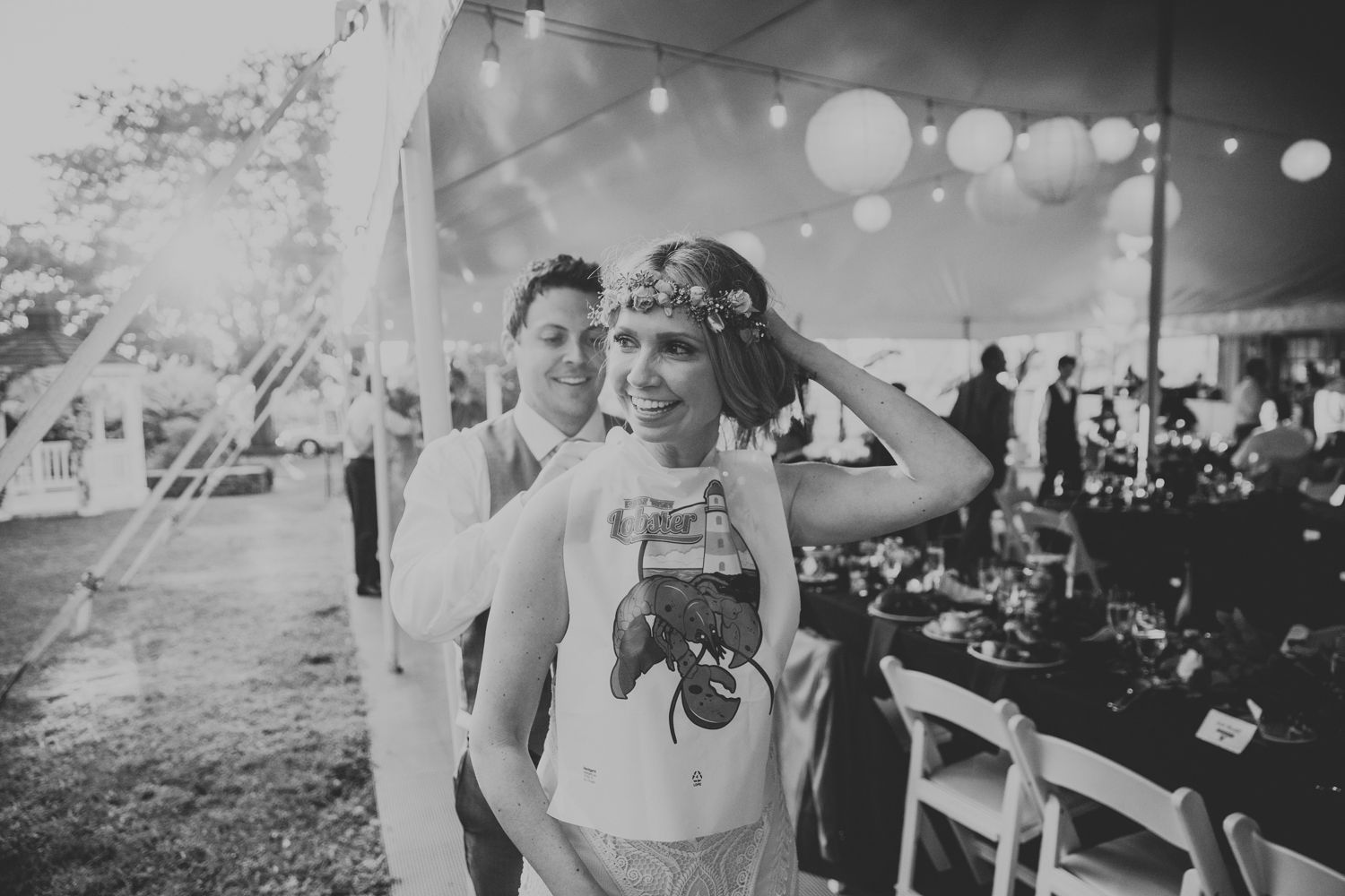 Black and white photo of two women smiling at an outdoor wedding reception under a tent with string lights.