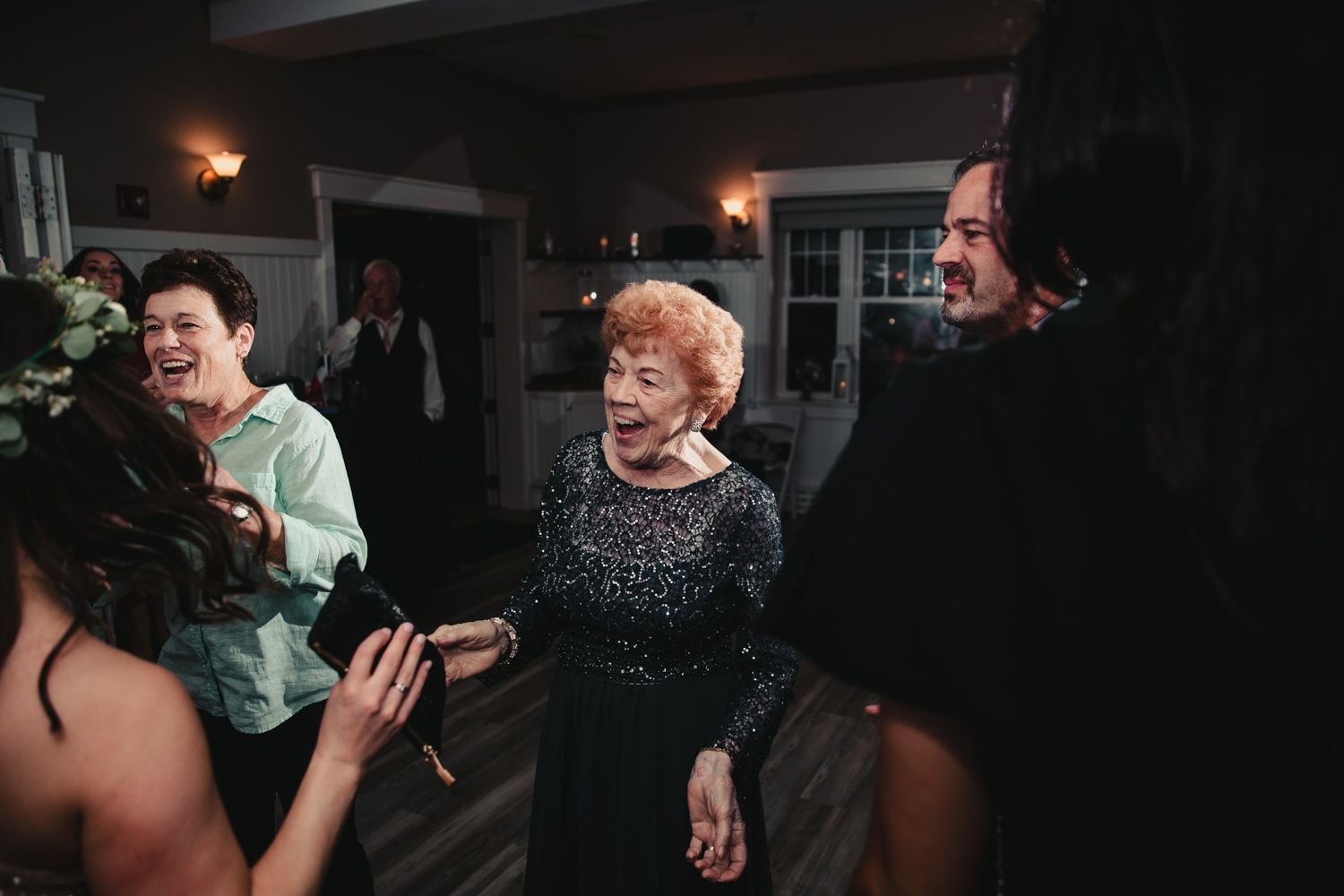 Elderly woman laughing joyfully with guests at an indoor wedding reception celebration.
