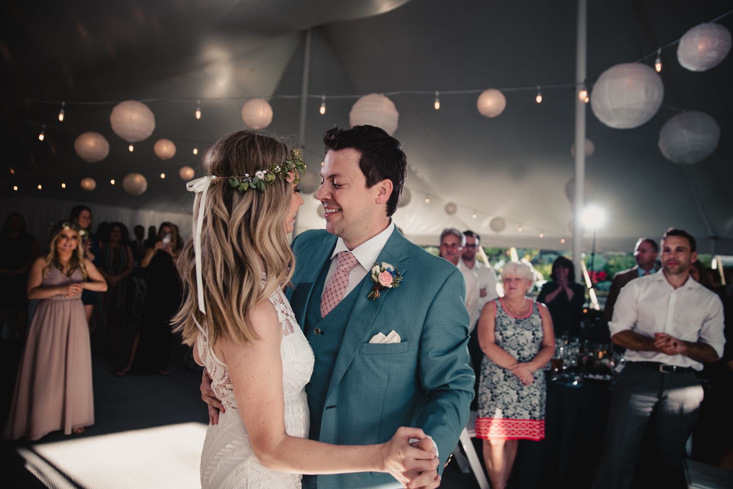 Bride and groom share first dance under string lights and paper lanterns at elegant tented wedding reception.