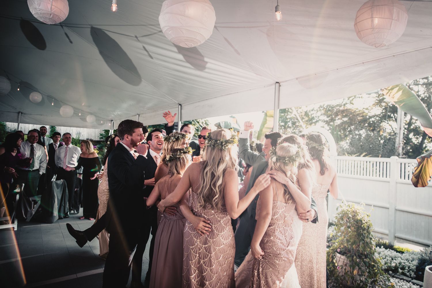 Wedding guests dancing under a white tent with paper lantern decorations at an elegant outdoor reception.