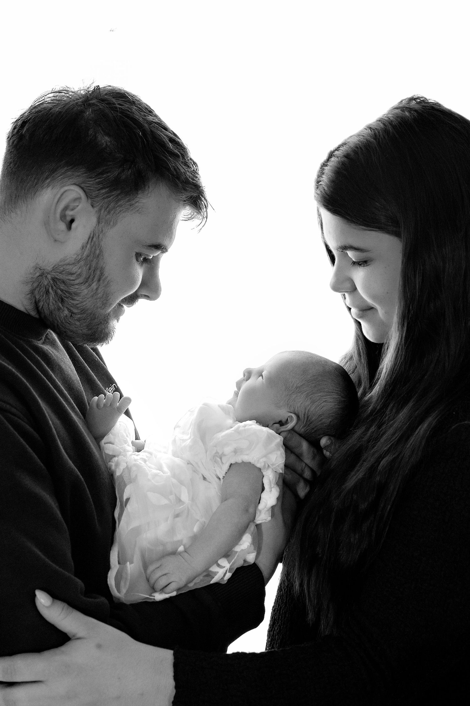 Black and white photo of new parents tenderly holding their newborn baby wrapped in white lace.