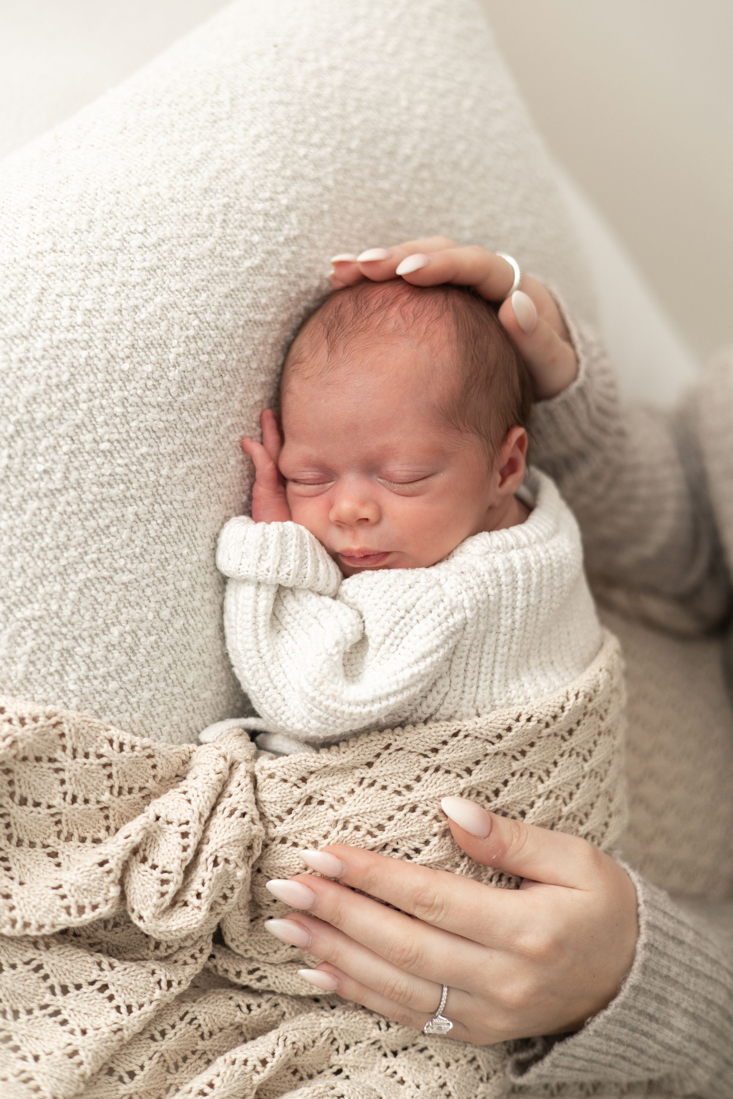 A sleeping newborn baby wrapped in a white knit blanket, cradled gently in a mother's hands, natural newborn photography Nottingham
