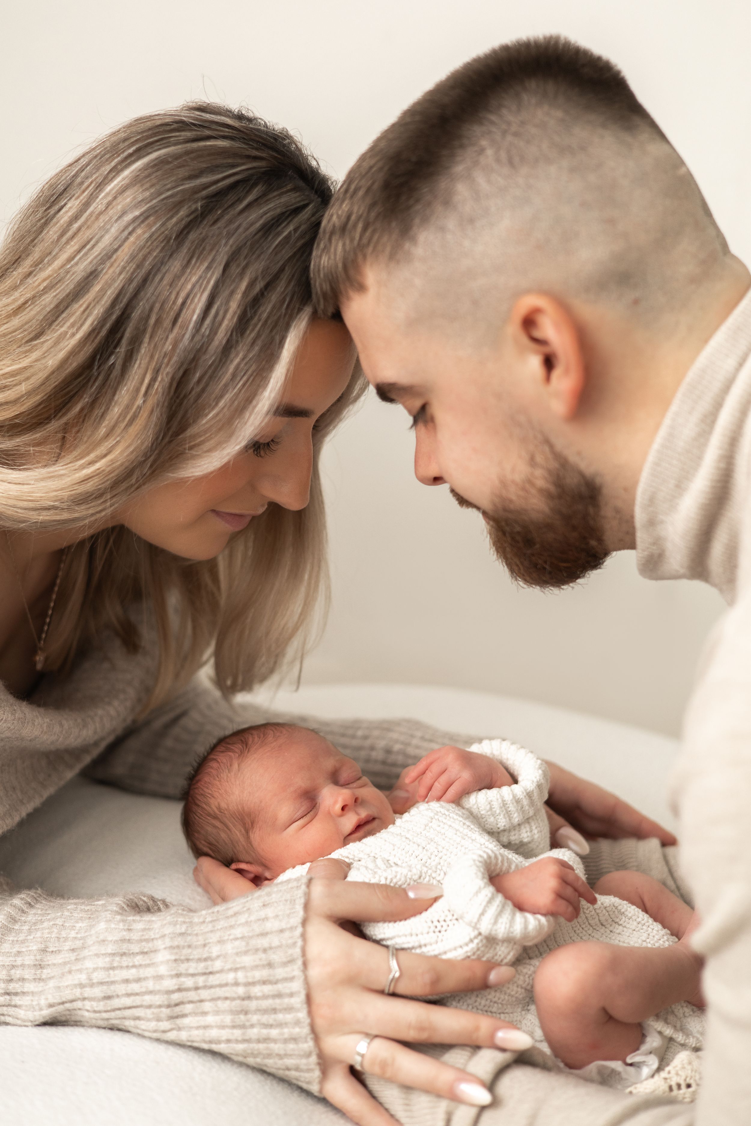 A young couple tenderly gazes at their sleeping newborn baby,  newborn family photography Nottingham