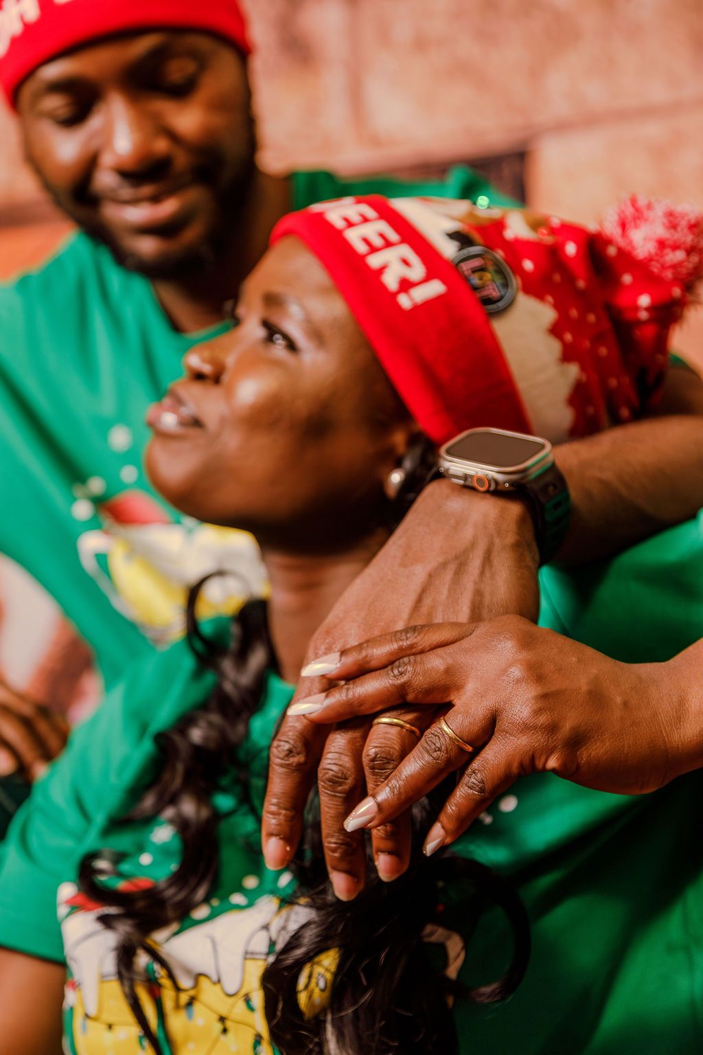 Couple in matching green Christmas shirts with red Oh Deer headbands sharing tender moment together.