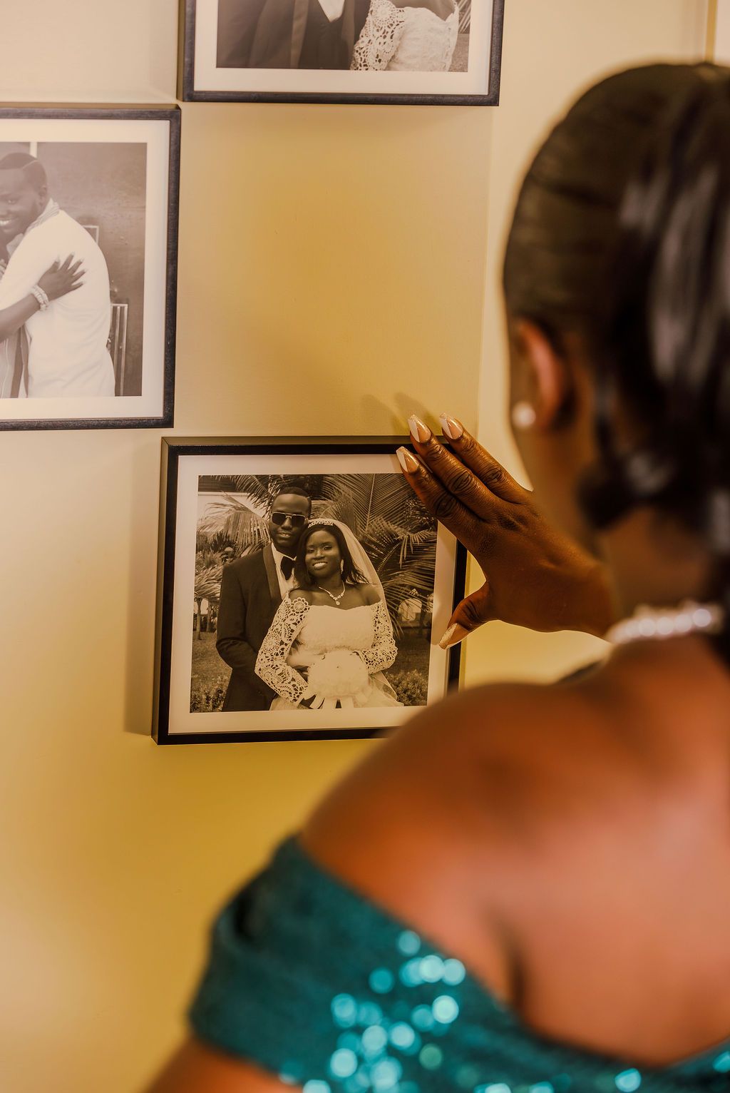 Woman in teal dress touching a framed black and white wedding photo on a wall.