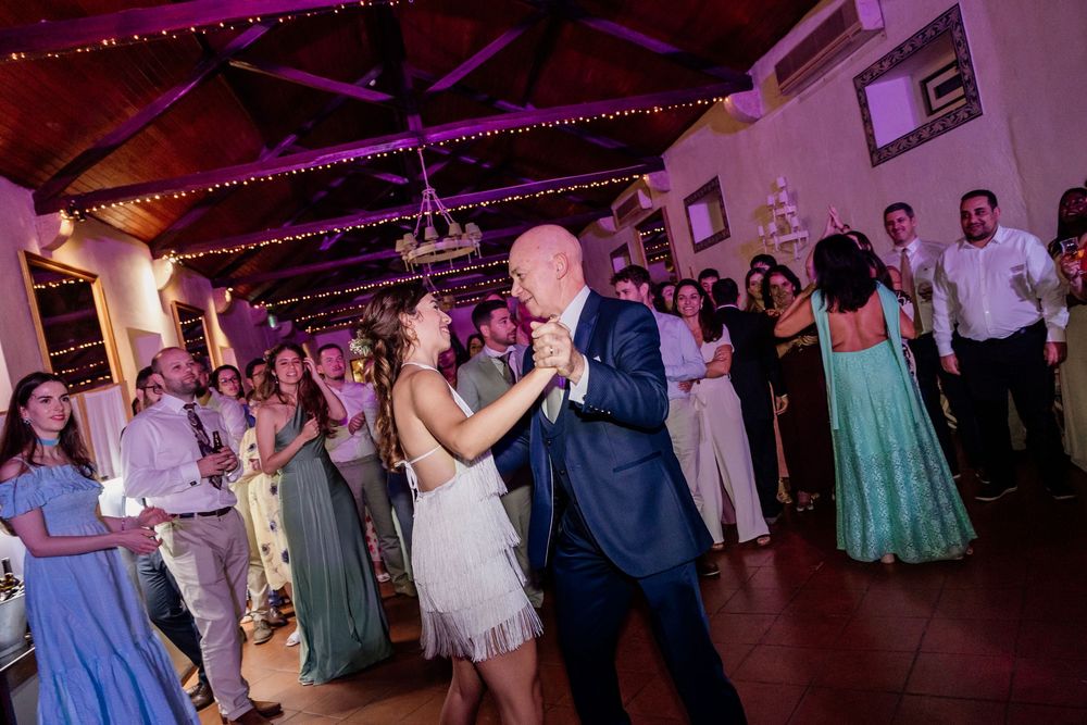 Couple shares first dance at wedding reception while guests clap and celebrate in decorated venue.