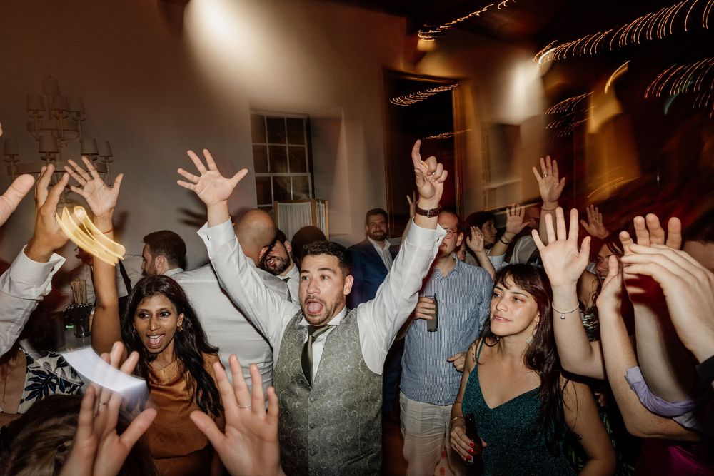 Excited wedding guests dancing with hands raised at a lively indoor wedding reception celebration.