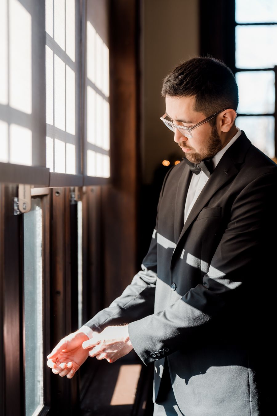 Groom adjusting cufflinks by window, in wedding attire at The Mansions On Fifth in Pittsburgh.