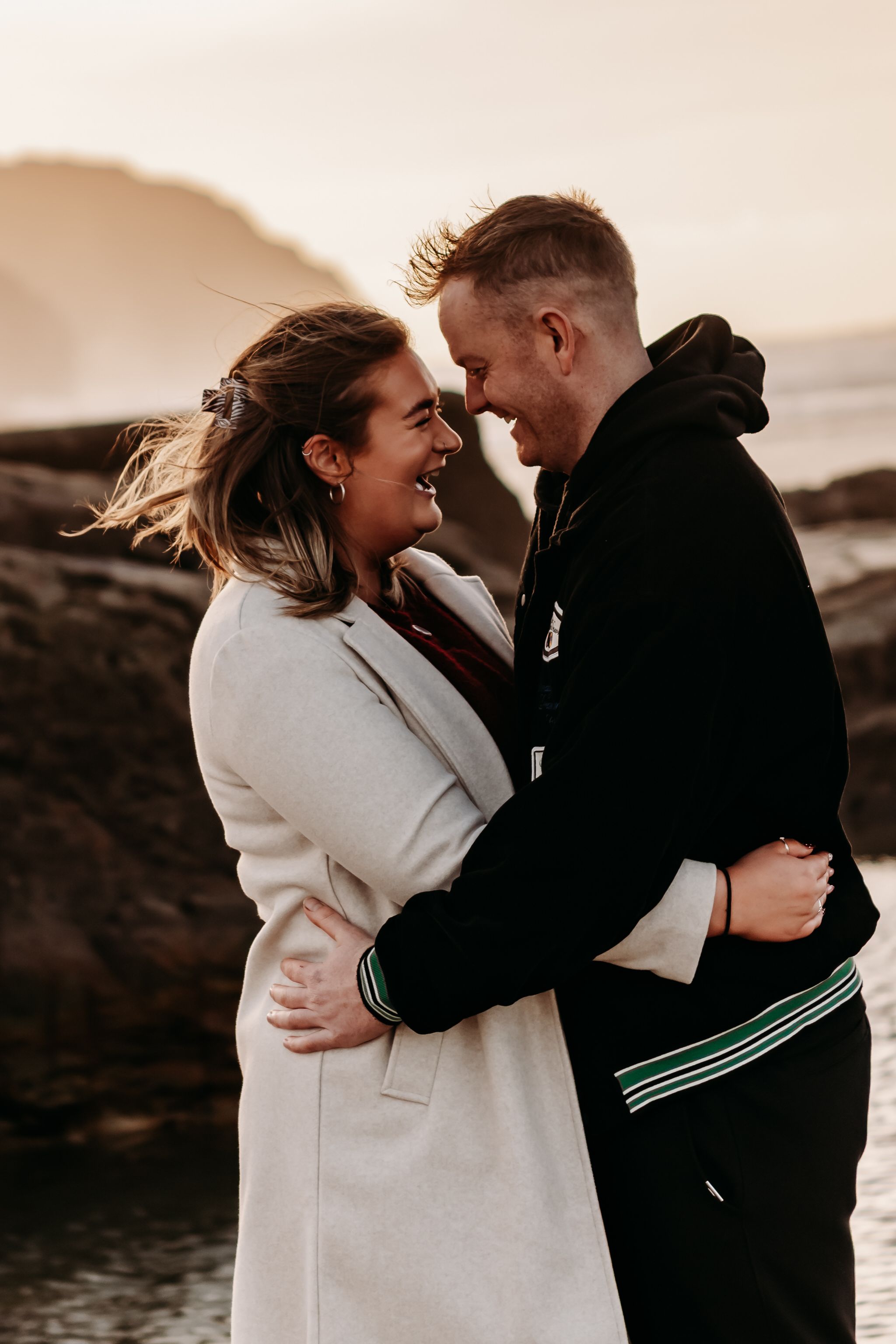A couple shares intimate moments at sunset on a rocky beach, captured in a series of romantic candid photographs.