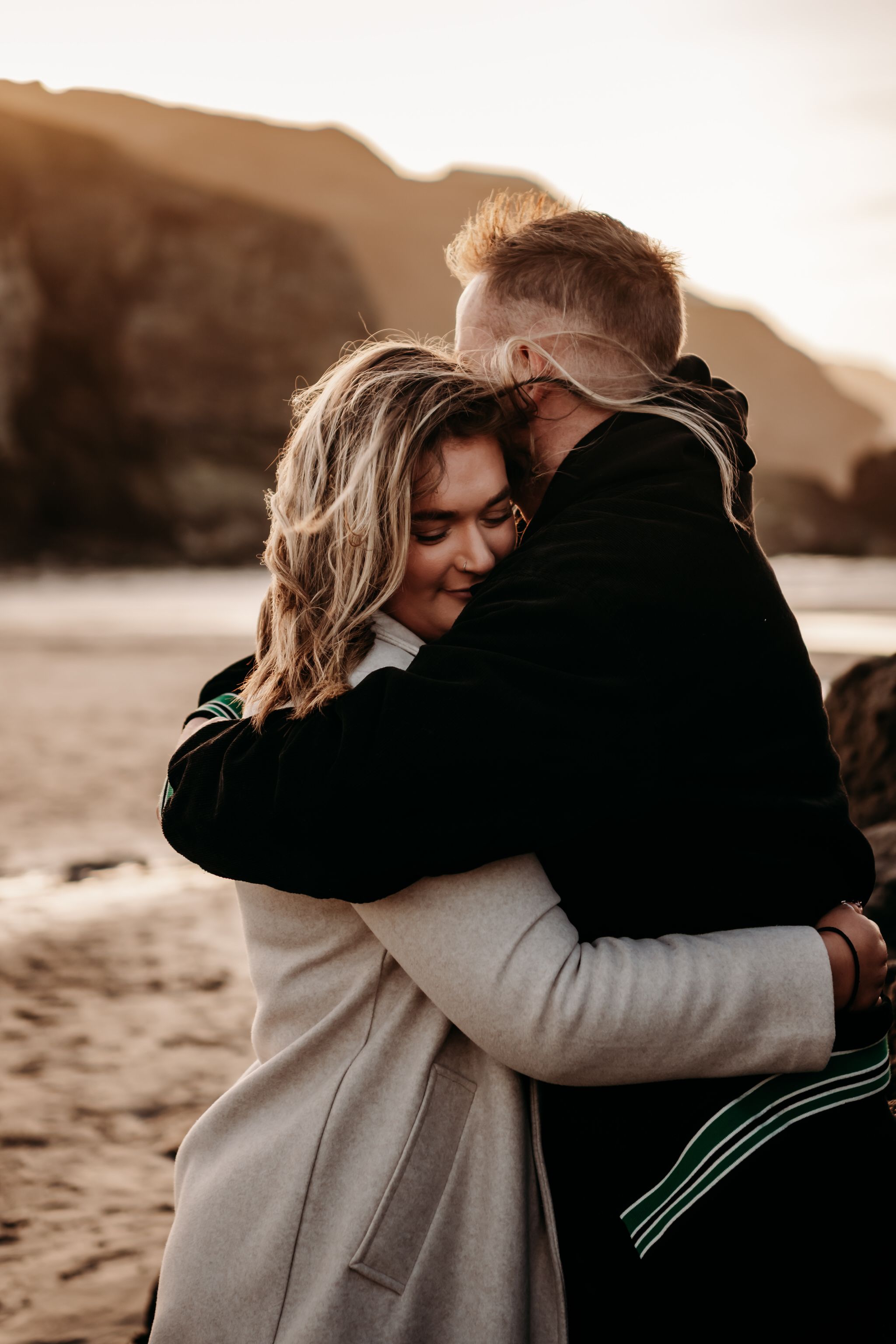 A couple embraces in a warm sunset glow on a beach, shown in a series of intimate moments captured in sepia tones.