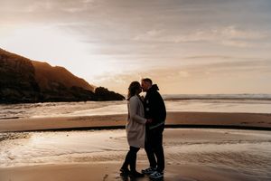 Silhouettes of a couple sharing romantic moments along a misty beach shoreline at sunset.