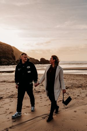 Two people share a tender moment while walking together on a moody beach at sunset.