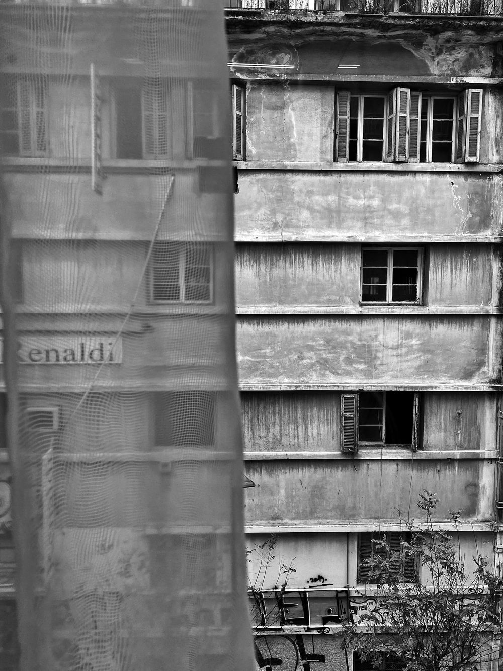 Black and white architectural photograph showing weathered apartment building facades with windows and balconies.