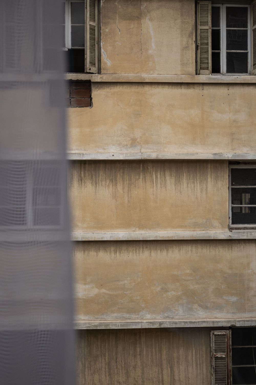 Exterior wall of a weathered beige apartment building with windows and horizontal architectural details.