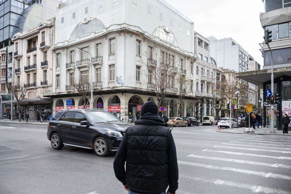 A black SUV drives through an urban intersection with historic buildings and pedestrians in the background.