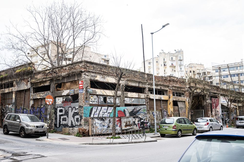 Panoramic urban street view showing multiple parked cars and graffiti-covered walls under an overpass structure.