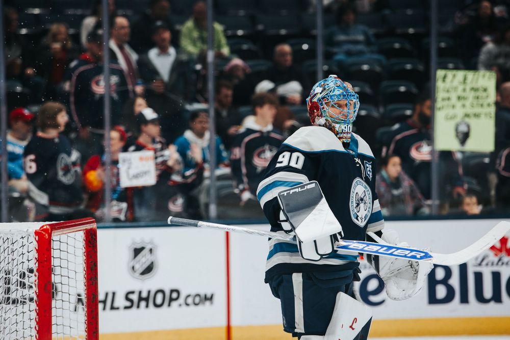 A hockey goalie makes a dramatic save while defending the net during an NHL game.
