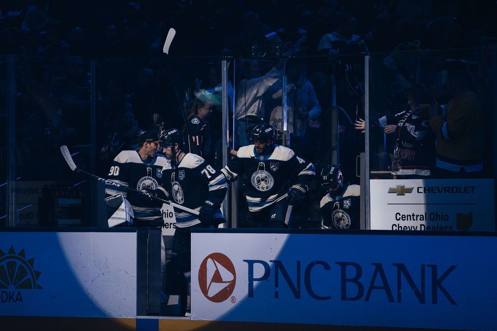 Silhouettes of hockey players skating on ice during a professional game with arena advertising boards visible in background.
