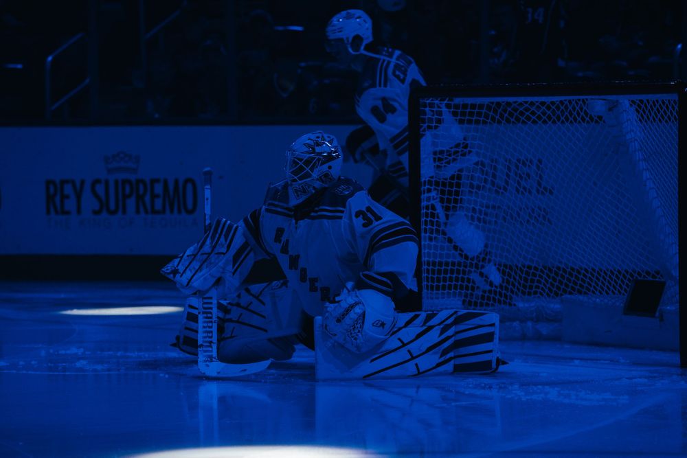 Ice hockey goalie makes a diving save attempt during a professional game under blue arena lighting.