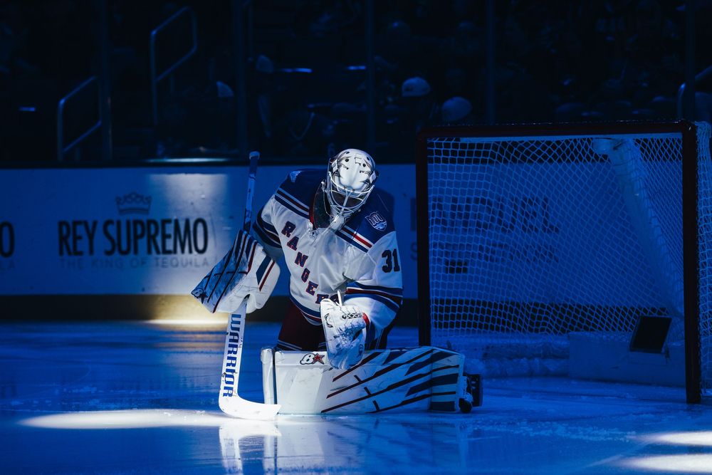 Hockey player in white jersey makes a dramatic save against the blue-lit backdrop of an ice rink.