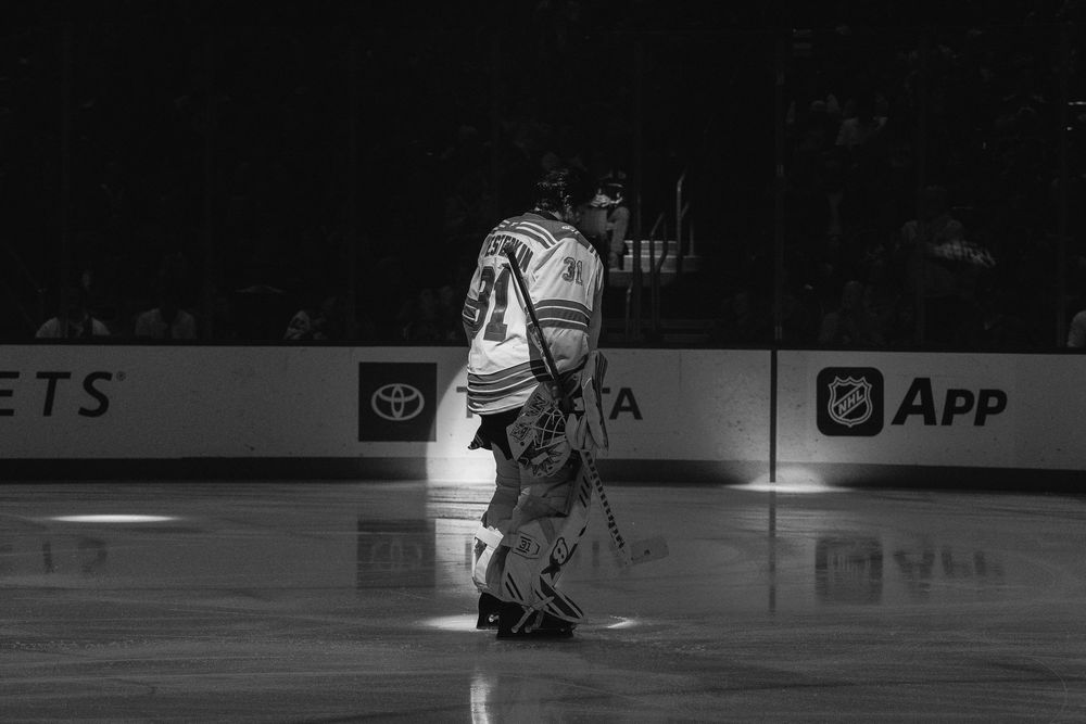 A hockey player in white jersey skates on ice during a competitive match with dramatic lighting.