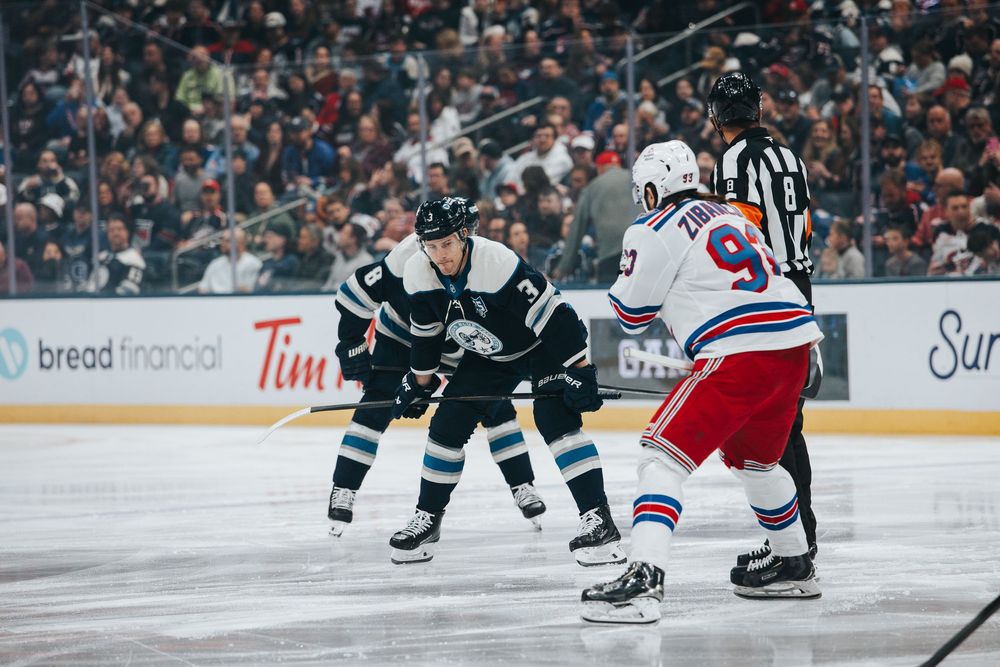 Professional hockey players from the Rangers and opposing team face off during an intense NHL game.