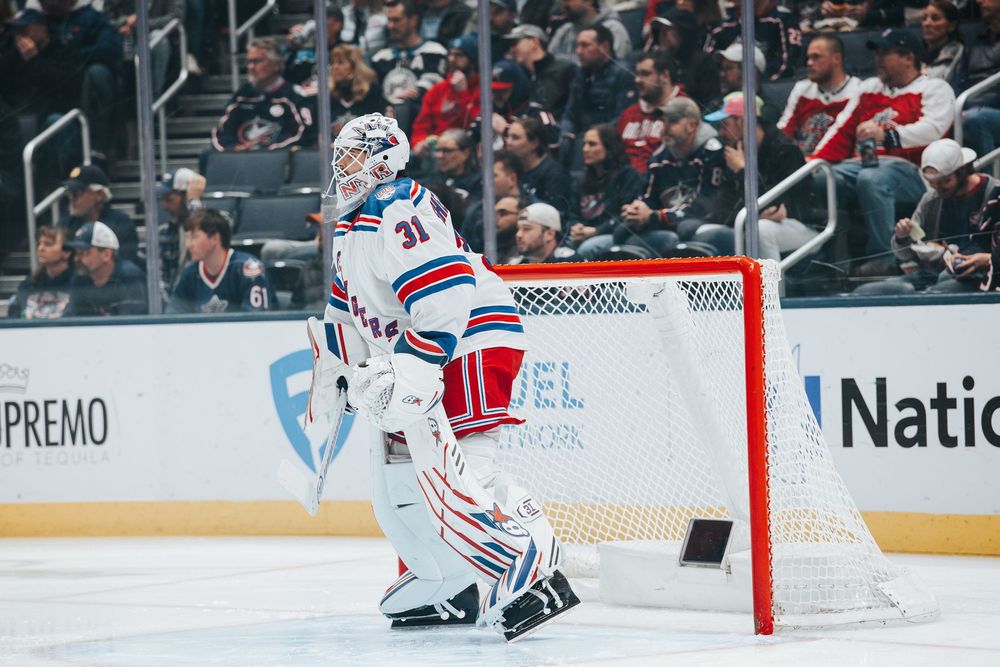 Hockey goalie in white and red uniform stands ready to defend the net during a professional game.