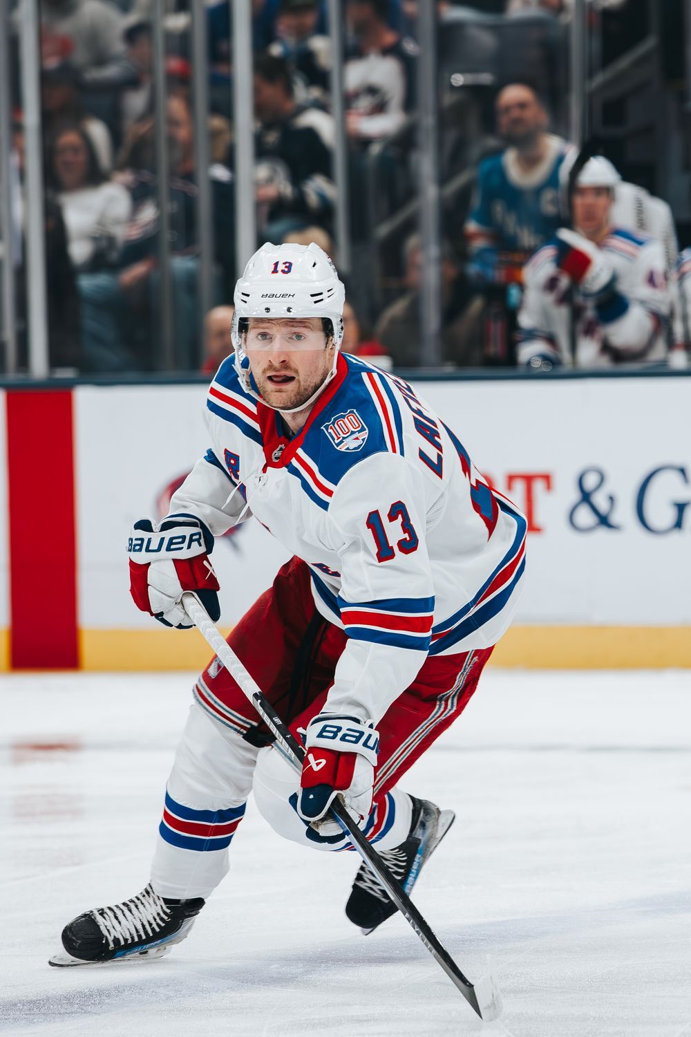 A hockey player in a New York Rangers white jersey number 13 skates with the puck during an NHL game.