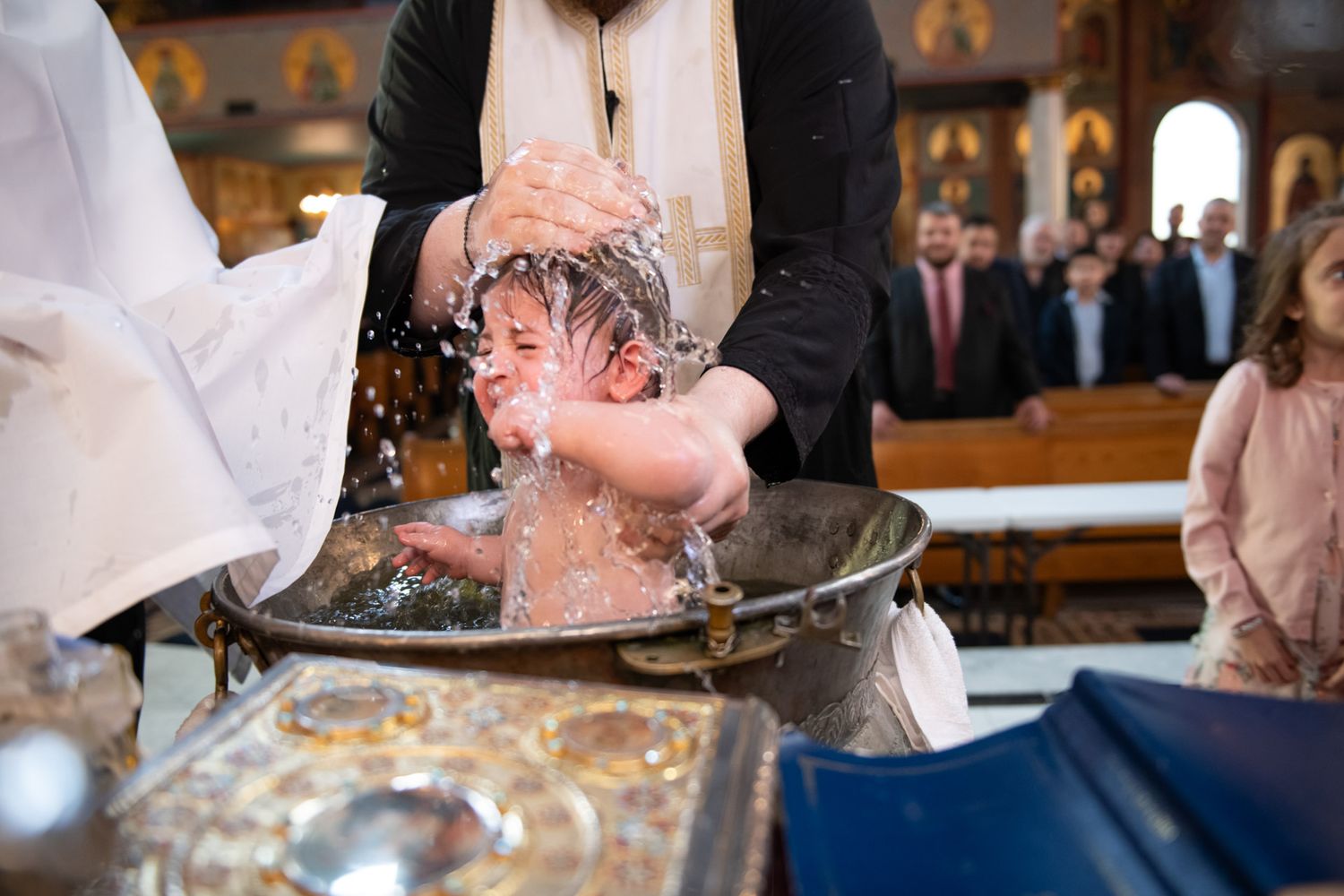 Baby being immersed in baptismal font during Orthodox Christian christening ceremony.