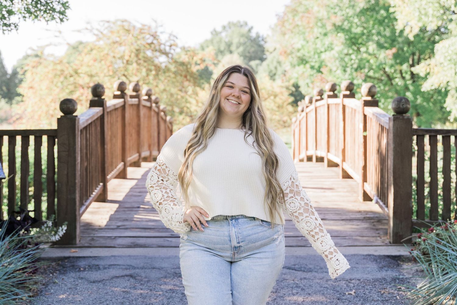 Toledo high school senior in white lace and denim poses on a wooden bridge walkway surrounded by autumn foliage.