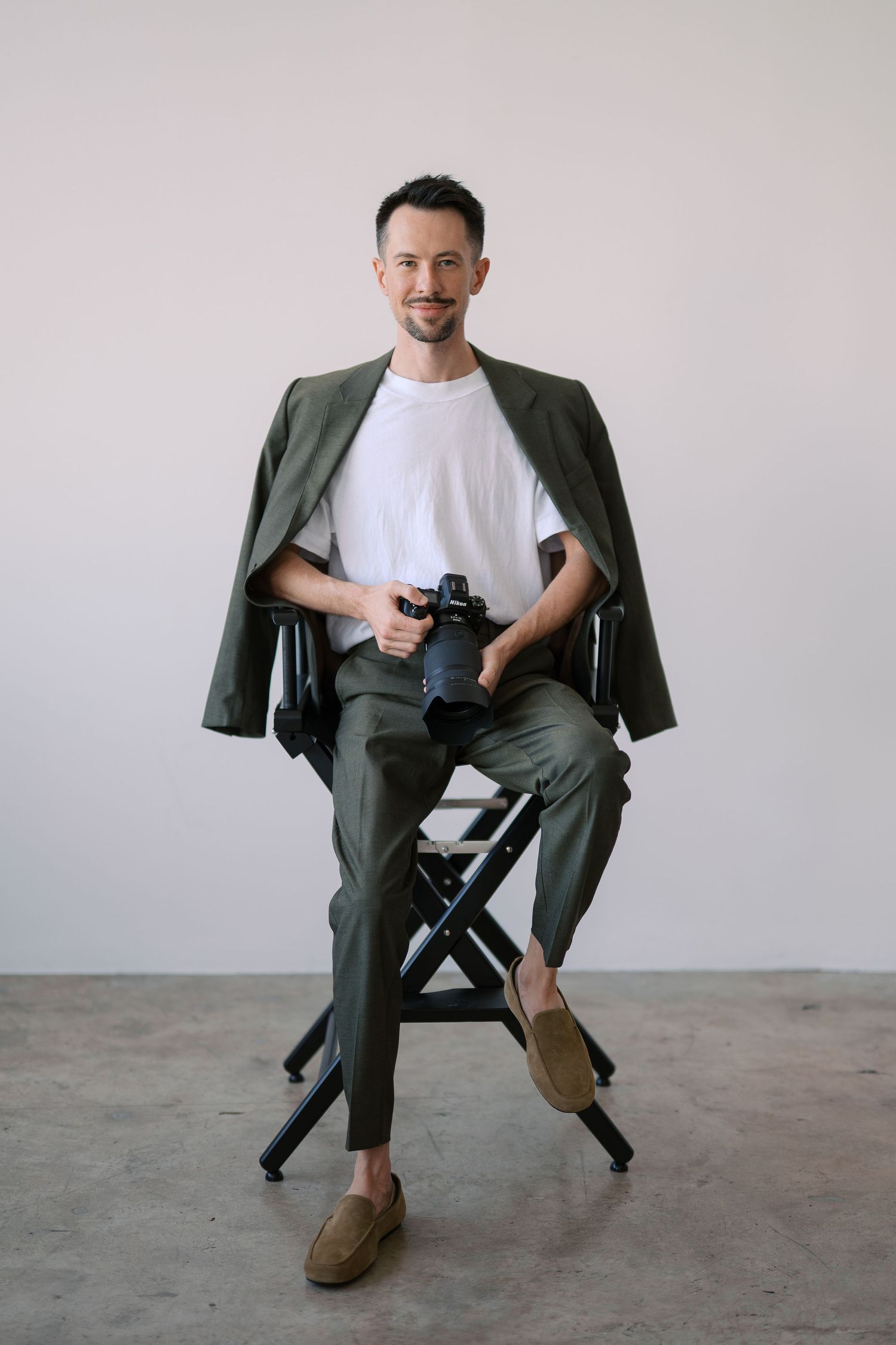 A person wearing a gray suit and white t-shirt poses casually in a chair against a light background in a photo series.