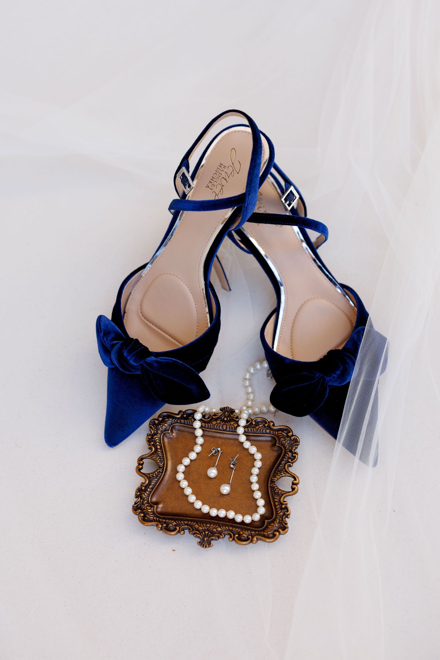 Navy blue velvet slingback heels with ornate gold buckle detail displayed on an antique bronze decorative tray.