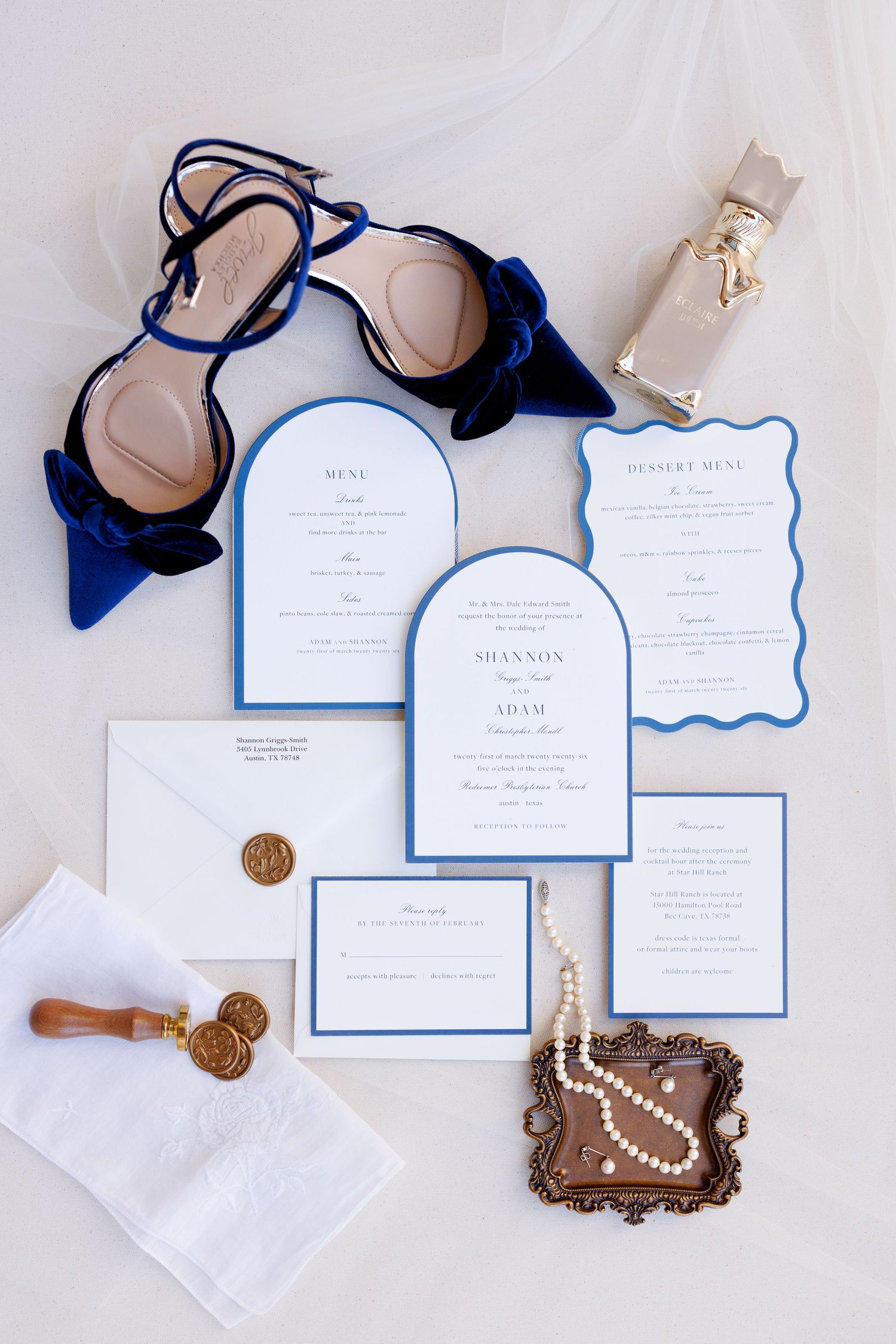 Elegant wedding invitation suite in white and navy blue with gold wax seals and pearl accessories laid flat on beige surface.