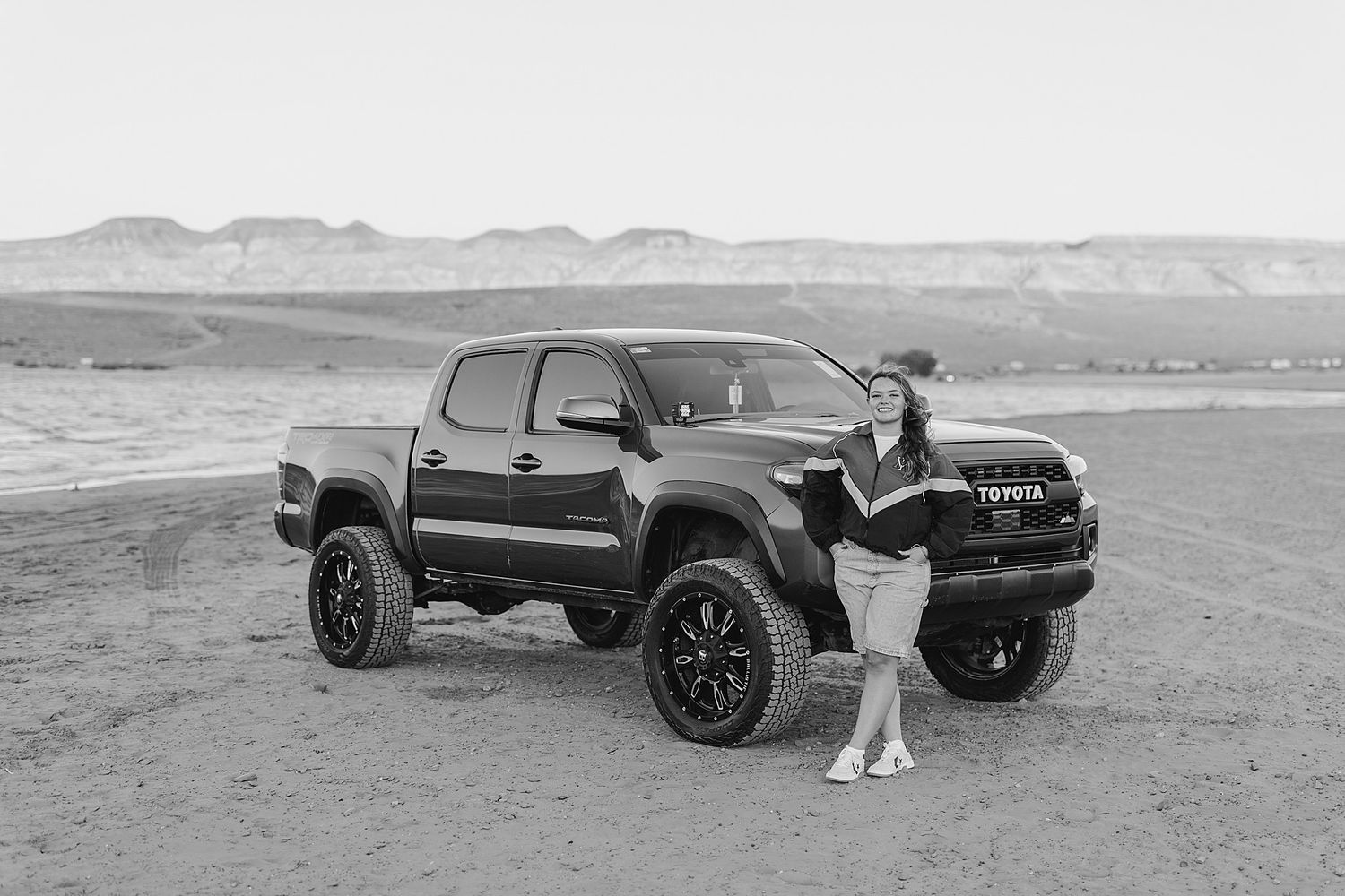 Woman posing beside a lifted black Toyota Tacoma truck in a desert landscape.