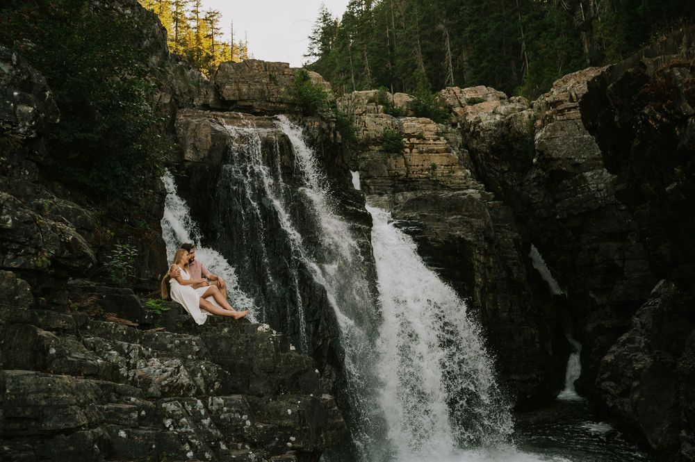 Couple adventure photoshoot session Vancouver island taken by professional photographer of couple sitting by lower Myra Waterfalls