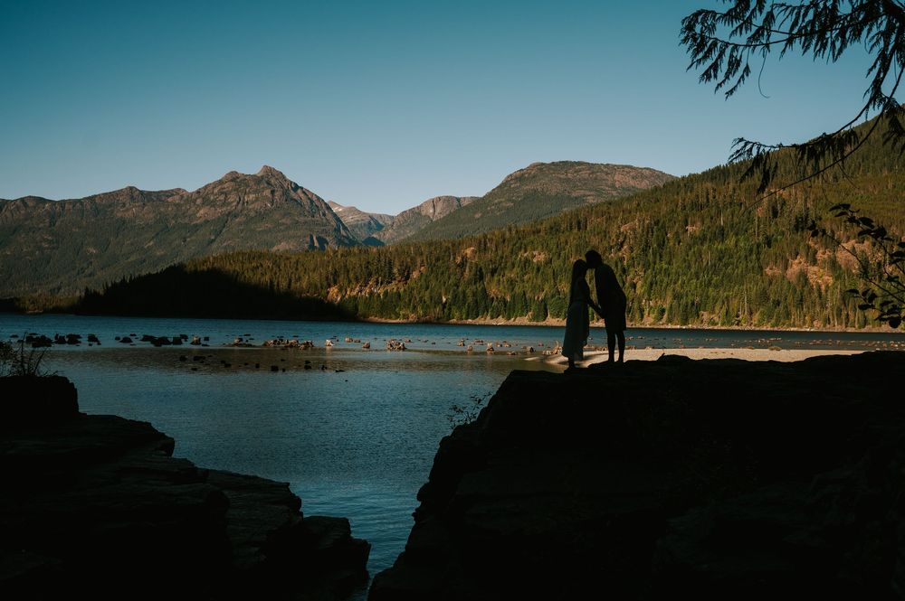 Couple adventure photoshoot Vancouver island taken by professional photographer of couple sitting by lower Myra Waterfalls Buttle lake
