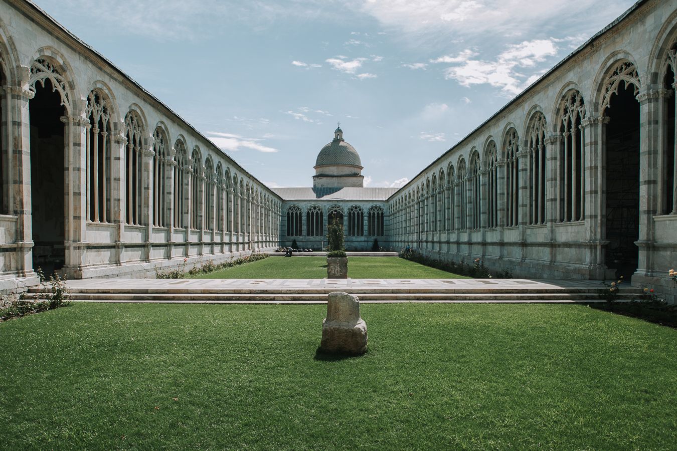 Symmetrical courtyard of historic Italian cemetery with arched colonnades and domed building in Pisa.