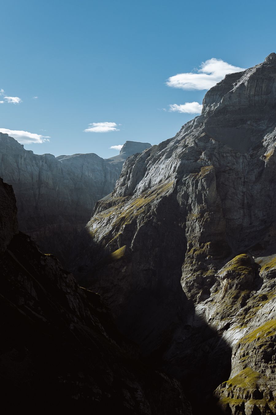 Dramatic rocky canyon walls bathed in sunlight with deep shadows under a blue sky.