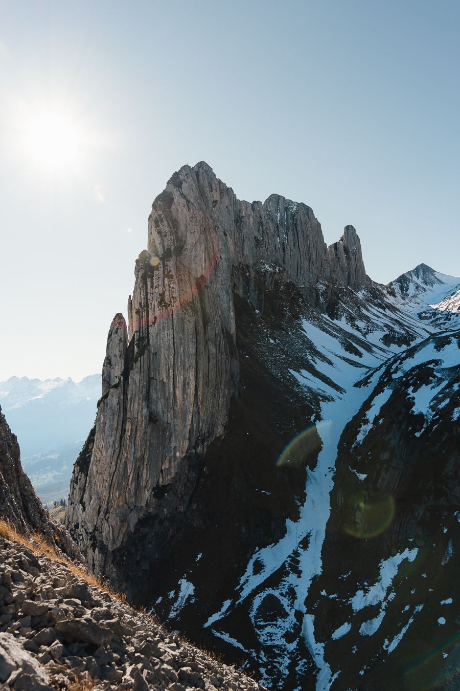Jagged rocky mountain spire with snow patches glowing in bright sunlight in the Alps.