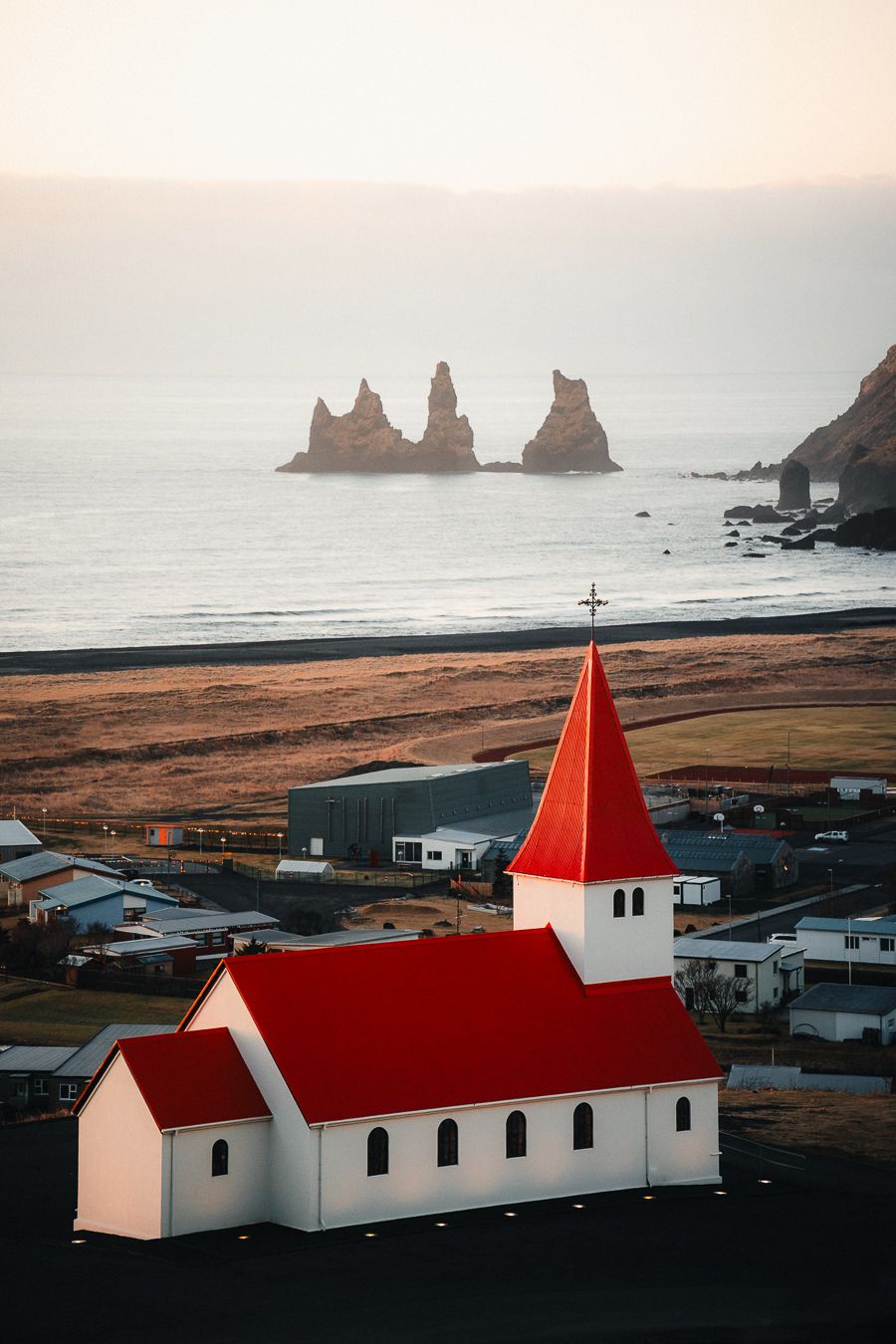 White church with red roof overlooking Vik village, black sand beach and Reynisdrangar sea stacks, Iceland.