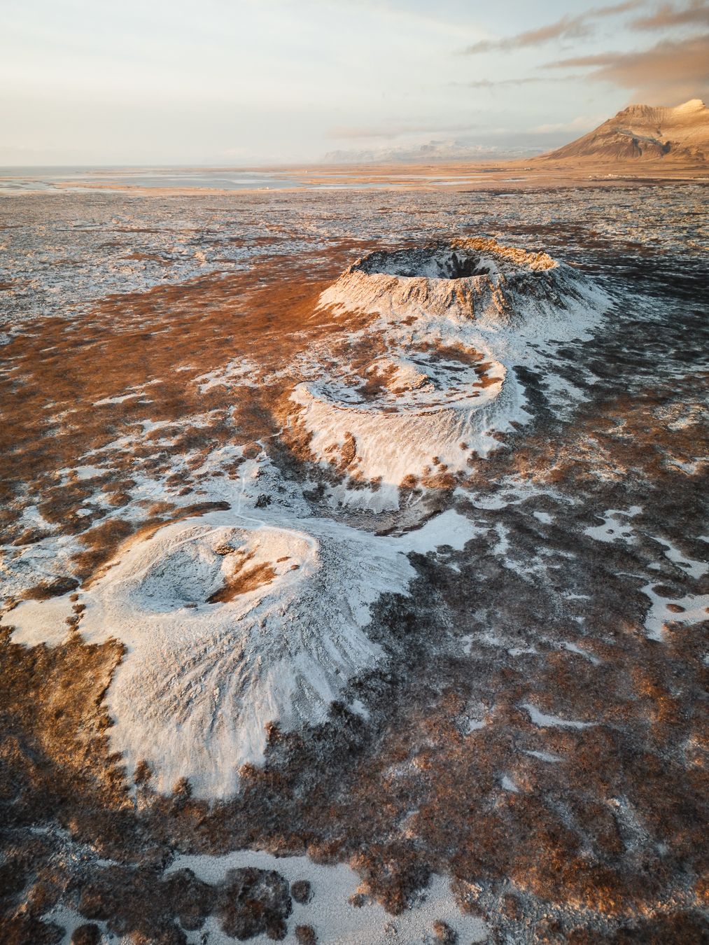 Aerial view of snow-dusted volcanic craters on Iceland's rugged lava field landscape at sunset.