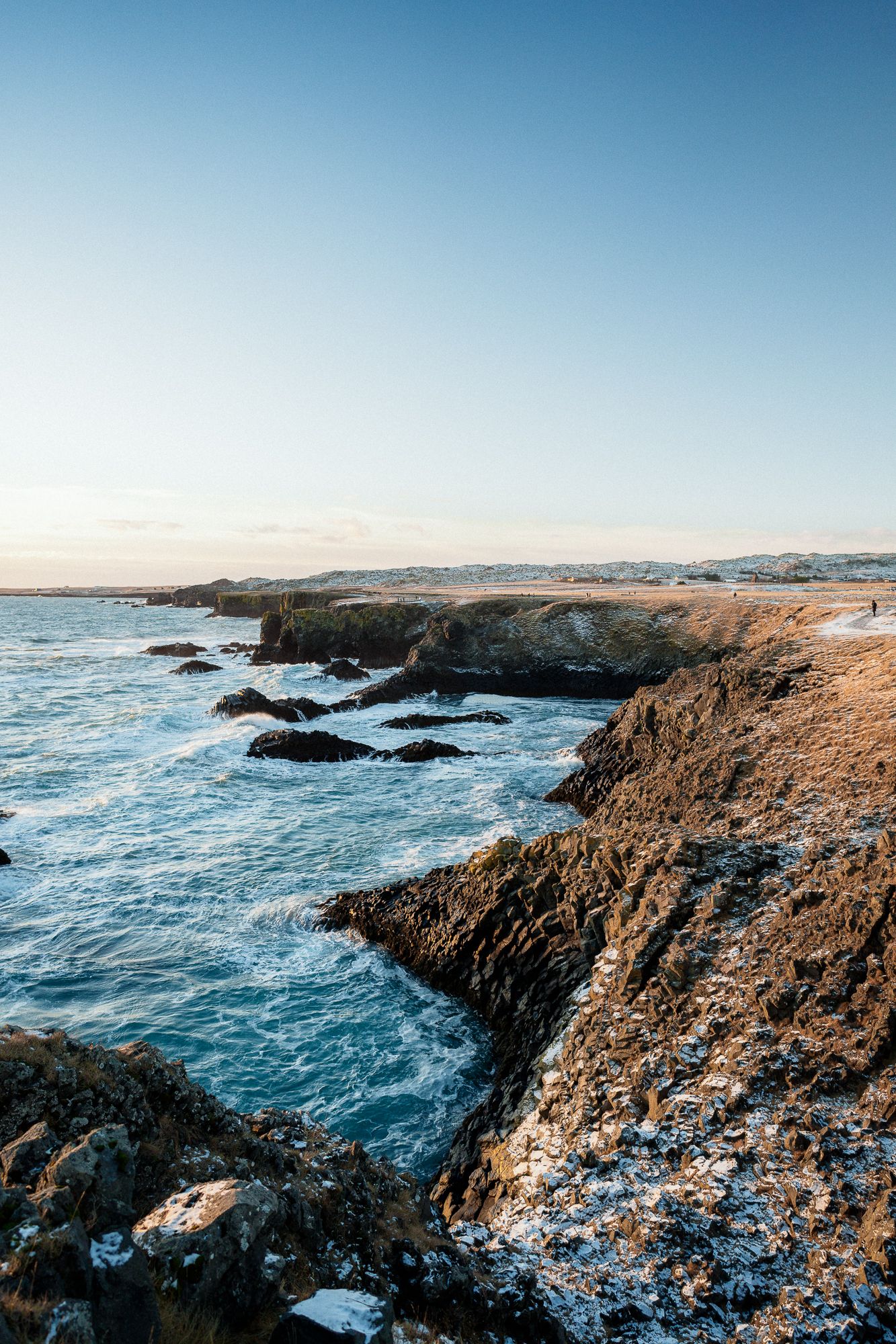 Rocky Atlantic coastline with crashing blue waves and cliffs stretching into the horizon at sunset.