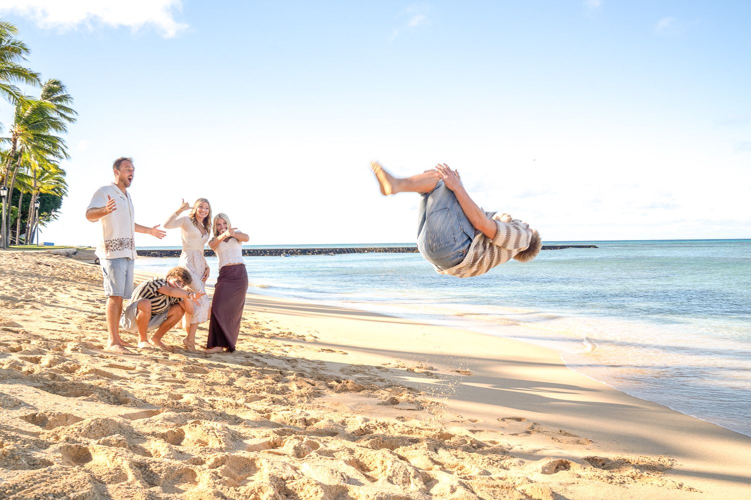 People doing acrobatic moves and flips on a tropical beach with palm trees and ocean waves in Hawaii.