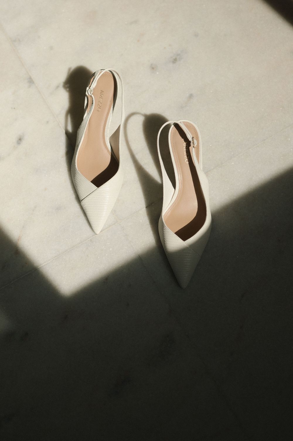 Elegant white bridal shoes cast dramatic shadows on a marble surface.