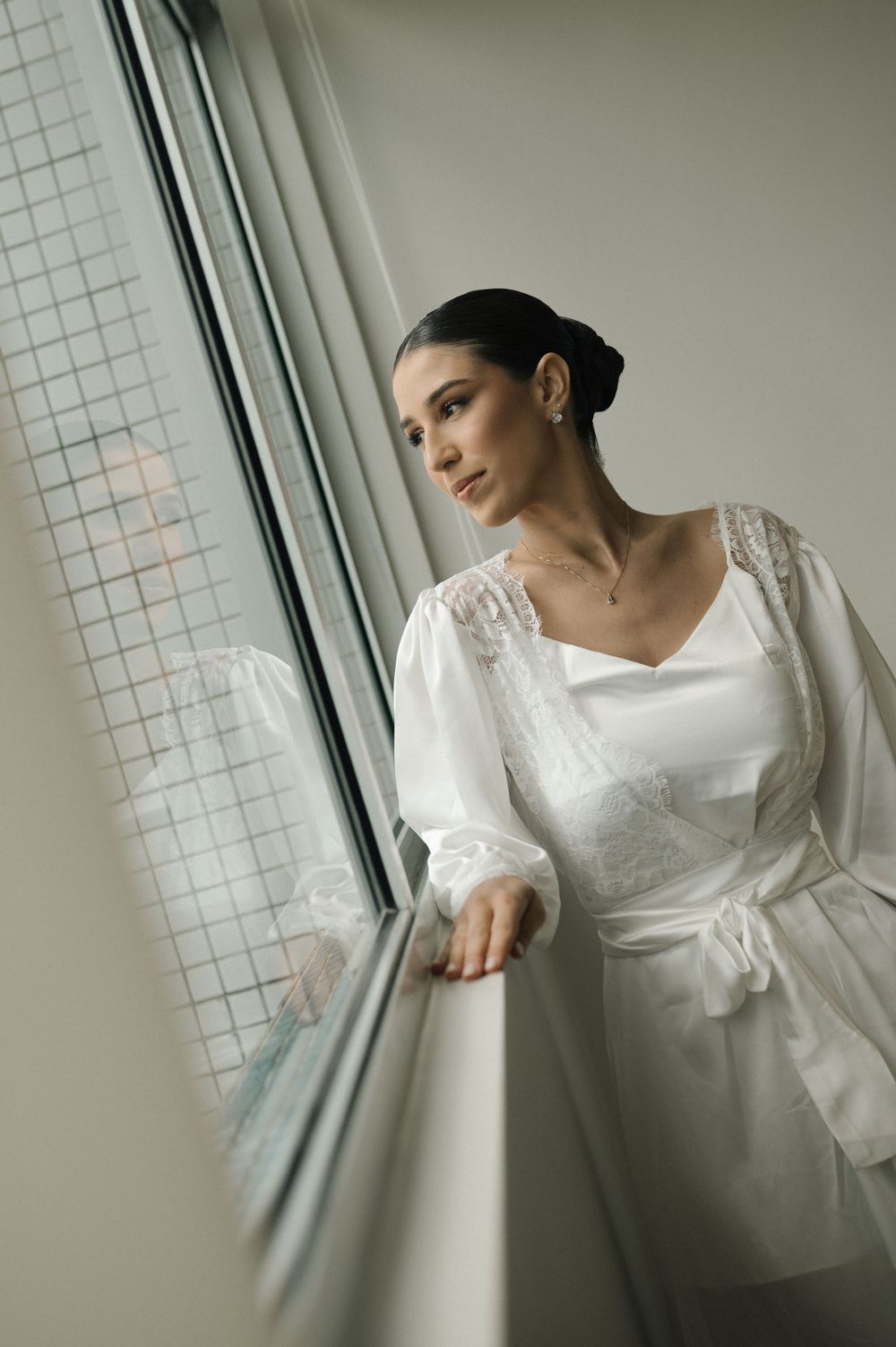 A person in a white vintage-style dress with puff sleeves poses gracefully by a window in soft natural light.