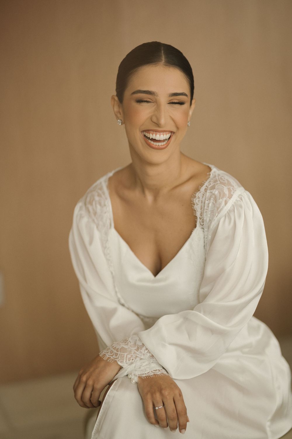 A joyful bride in a white dress with puff sleeves laughs candidly against a neutral background.
