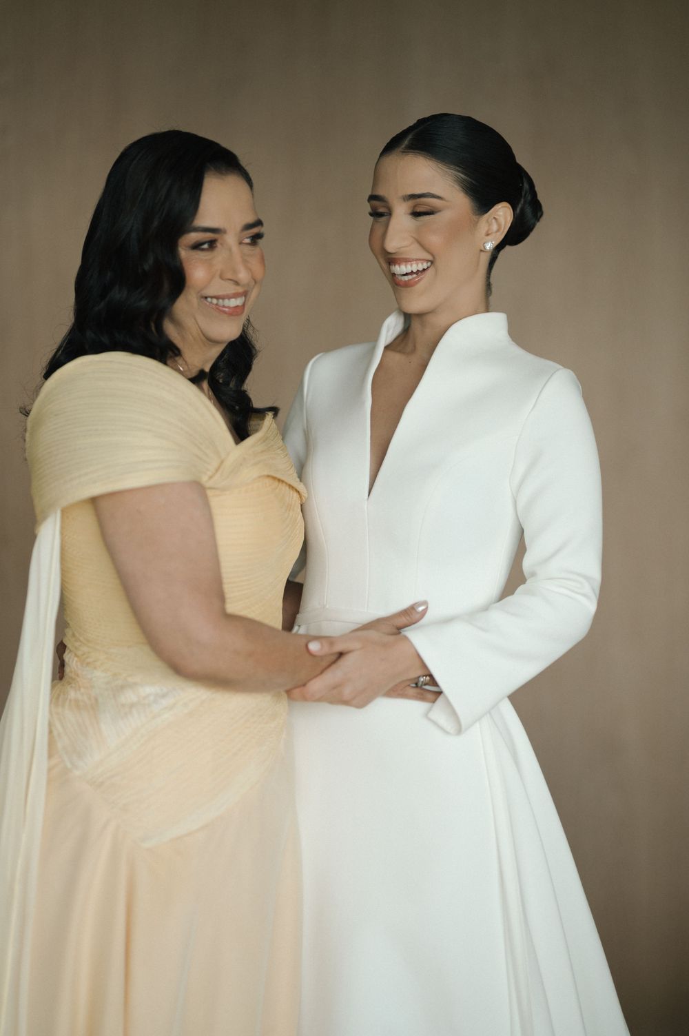 Two people in contrasting white and cream formal attire share a joyful moment together.