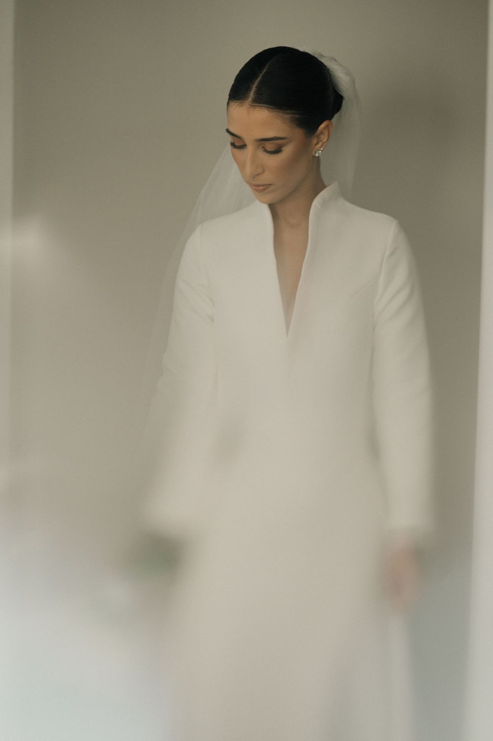 A figure in an elegant white garment stands near a window creating a dreamy, minimalist portrait composition.